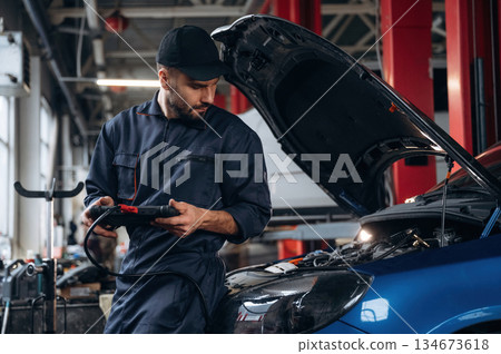 Electronics adjustment, with digital tablet. Mechanic working in a car service station Electronics adjustment, with digital tablet. Mechanic working in a car service station 134673618