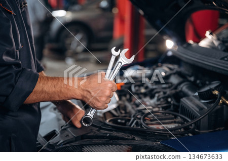 Tools in hand. Close up view of mechanic in car service station 134673633