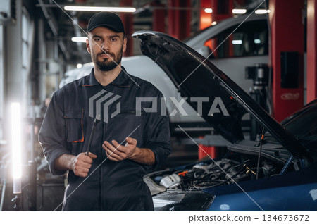 Front view, standing and holding tool. Mechanic working in a car service station Front view, standing and holding tool. Mechanic working in a car service station 134673672