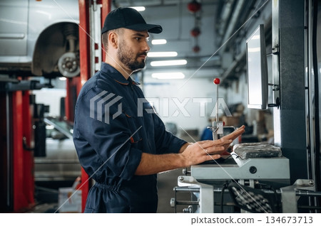 Standing by the display. Mechanic working in a car service station Standing by the display. Mechanic working in a car service station 134673713