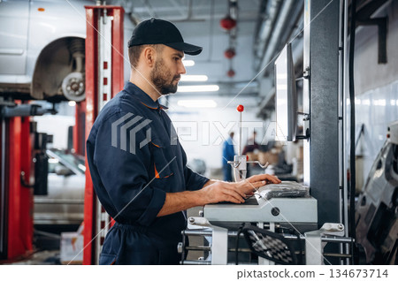 Standing by the display. Mechanic working in a car service station Standing by the display. Mechanic working in a car service station 134673714