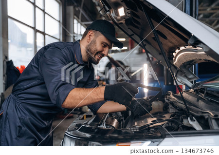 Smiling, cheerful facial expression. Mechanic working in a car service station Smiling, cheerful facial expression. Mechanic working in a car service station 134673746