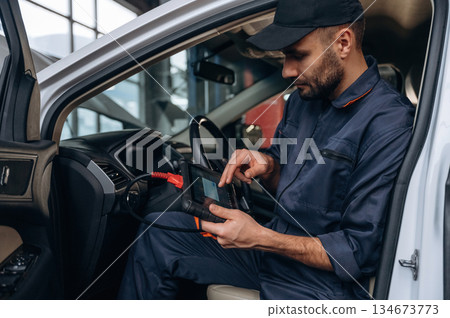 On the seat, with digital tablet. Mechanic working in a car service station 134673773
