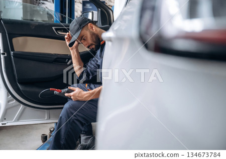 Break time, sitting in automobile. Mechanic working in a car service station Break time, sitting in automobile. Mechanic working in a car service station 134673784