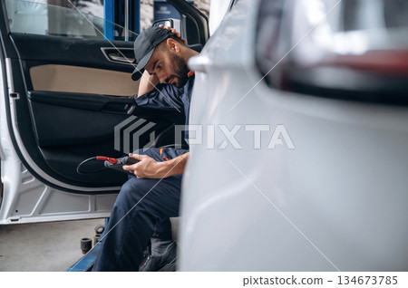 Break time, sitting in automobile. Mechanic working in a car service station Break time, sitting in automobile. Mechanic working in a car service station 134673785