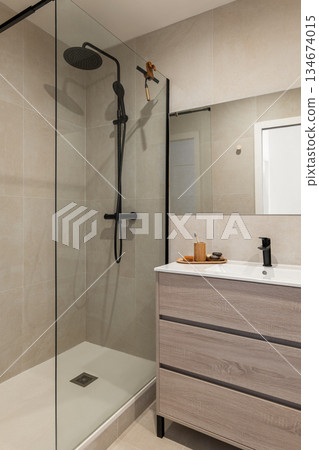 Modern bathroom with a glass shower enclosure, wooden vanity, and minimalist decor. Neutral color palette creates a serene atmosphere. Modern bathroom with a glass shower enclosure, wooden vanity, and minimalist decor. Neutral color palette creates a serene atmosphere. 134674015