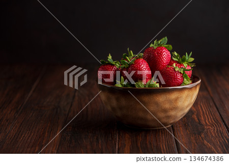 Fresh red strawberries in a rustic bowl on a dark wooden background. Front view 134674386