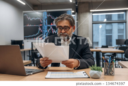 Boring work, sitting by the laptop. Senior man is in the modern office Boring work, sitting by the laptop. Senior man is in the modern office 134674397