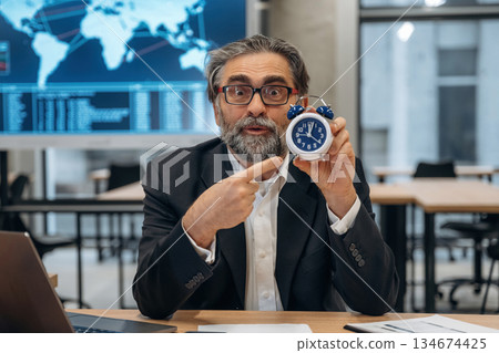 Time is running out, holding clock. Senior man is in the modern office Time is running out, holding clock. Senior man is in the modern office 134674425