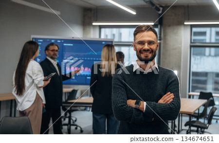 With arms crossed, standing against colleagues. Group of office workers are indoors together 134674651