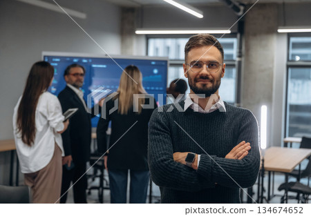 With arms crossed, standing against colleagues. Group of office workers are indoors together 134674652