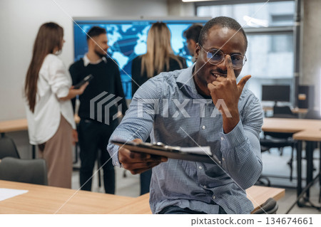Black man is with notepad. Group of office workers are indoors together Black man is with notepad. Group of office workers are indoors together 134674661