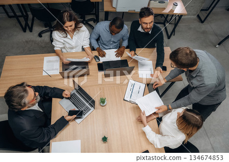 Top view, sitting by the table. Group of office workers are indoors together Top view, sitting by the table. Group of office workers are indoors together 134674853