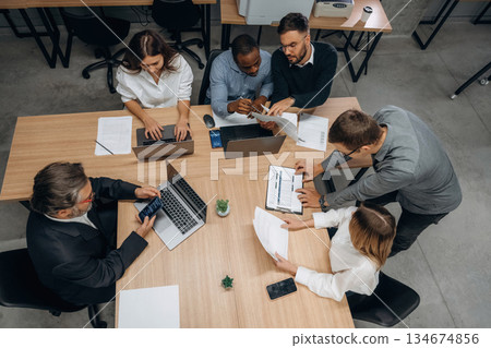 Top view, sitting by the table. Group of office workers are indoors together Top view, sitting by the table. Group of office workers are indoors together 134674856