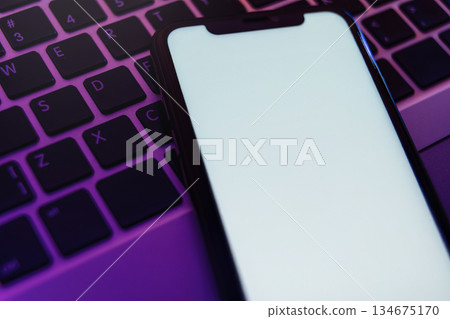 Blank white smartphone display on illuminated computer keyboard in neon light 134675170