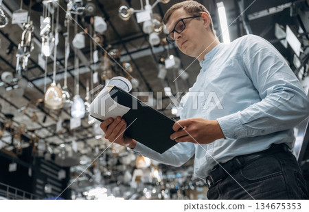 Many chandeliers on the ceiling. Male hardware store worker in indoors Many chandeliers on the ceiling. Male hardware store worker in indoors 134675353