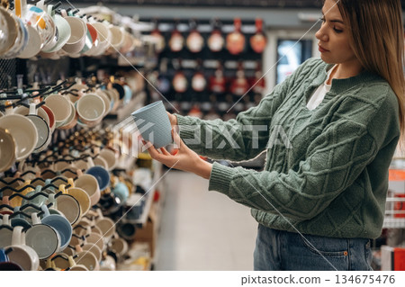 Standing, holding new cups. Woman is in the hardware store, shopping conception Standing, holding new cups. Woman is in the hardware store, shopping conception 134675476