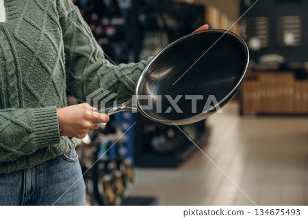 Quality new black pan. Close up view of woman that is in the hardware store Quality new black pan. Close up view of woman that is in the hardware store 134675493