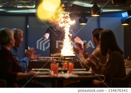Family gathers around while chef prepares fiery dish during iftar meal celebration in restaurant for Ramadan 134676341