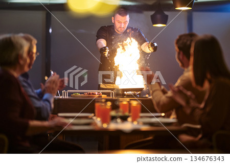 Family gathers around a table to watch a chef perform cooking tricks during iftar at a restaurant in Ramadan Family gathers around a table to watch a chef perform cooking tricks during iftar at a restaurant in Ramadan 134676343