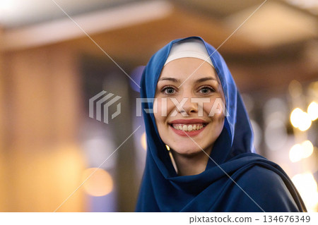 Woman wearing a blue hijab smiles during family iftar gathering in Ramadan at a decorated restaurant Woman wearing a blue hijab smiles during family iftar gathering in Ramadan at a decorated restaurant 134676349