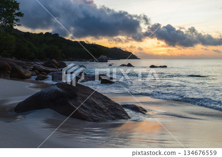 A peaceful coastal scene at sunset features smooth sand and rocks A peaceful coastal scene at sunset features smooth sand and rocks 134676559