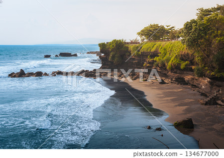 Tanah Lot coast quiet bay with dark sand beach and green cliffs near Bali temple area offers peaceful ocean scenery, tropical shoreline, soft waves Bali natural travel atmosphere high quality photo Tanah Lot coast quiet bay with dark sand beach and green cliffs near Bali temple area offers peaceful ocean scenery, tropical shoreline, soft waves Bali natural travel atmosphere high quality photo 134677000