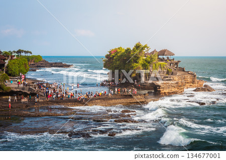Tanah Lot temple iconic Hindu shrine on rocky island in Bali draws visitors with ocean waves, sacred architecture, tropical coast and spiritual travel atmosphere during daylight. High quality photo 134677001