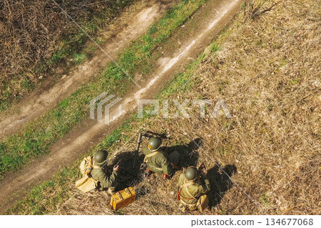 Men Dressed As US American Soldiers Of USA Infantry Of World War II sneaking around In spring Autumn Day. Soldiers prepare mortar for battle In dry grass. Aerial view elevated shot Men Dressed As US American Soldiers Of USA Infantry Of World War II sneaking around In spring Autumn Day. Soldiers prepare mortar for battle In dry grass. Aerial view elevated shot 134677068