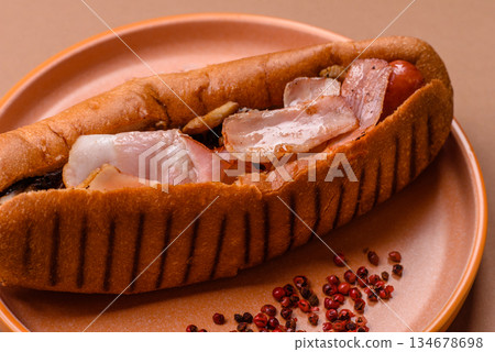 A hot dog with sausage, bacon, sauces, and a bun, unhealthy takeaway food. A hot dog with bacon A hot dog with sausage, bacon, sauces, and a bun, unhealthy takeaway food. A hot dog with bacon 134678698