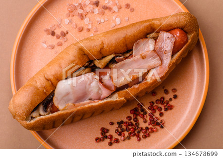 A hot dog with sausage, bacon, sauces, and a bun, unhealthy takeaway food. A hot dog with bacon A hot dog with sausage, bacon, sauces, and a bun, unhealthy takeaway food. A hot dog with bacon 134678699