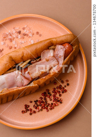 A hot dog with sausage, bacon, sauces, and a bun, unhealthy takeaway food. A hot dog with bacon A hot dog with sausage, bacon, sauces, and a bun, unhealthy takeaway food. A hot dog with bacon 134678700
