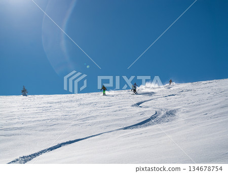 Three skiers carve down a sunny, powder-covered mountain slope, kicking up fresh snow under a clear blue sky, creating a dynamic winter sports action scene Three skiers carve down a sunny, powder-covered mountain slope, kicking up fresh snow under a clear blue sky, creating a dynamic winter sports action scene 134678754
