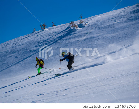 Three skiers carve down a sunny, powder-covered mountain slope, kicking up fresh snow under a clear blue sky, creating a dynamic winter sports action scene Three skiers carve down a sunny, powder-covered mountain slope, kicking up fresh snow under a clear blue sky, creating a dynamic winter sports action scene 134678766