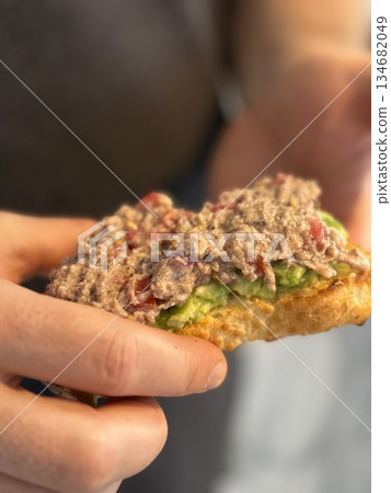 Hands holding tuna and avocado open sandwich with blurred background Hands holding tuna and avocado open sandwich with blurred background 134682049