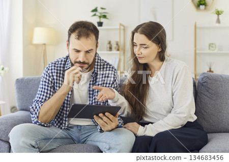 Couple browsing on tablet at home, searching options together on cozy sofa Couple browsing on tablet at home, searching options together on cozy sofa 134683456