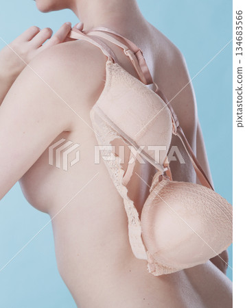 Naked woman holds beige bra in hand Naked woman holds beige bra in hand 134683566