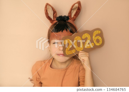 A narrowed, sly girl looks out with interest from behind the numbers 2026. New Year of the Fiery Horse 134684765