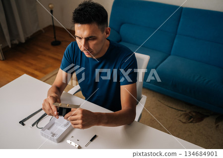 High-angle view of technician male assembling wi-fi module using tools at home office desk, focusing on intricate components and ensuring proper connection. Concept of desktop PC maintenance High-angle view of technician male assembling wi-fi module using tools at home office desk, focusing on intricate components and ensuring proper connection. Concept of desktop PC maintenance 134684901