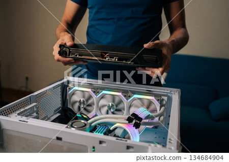 Computer technician installing powerful new graphic card into custom-built gaming pc, featuring vibrant RGB lighting and advanced water cooling system for optimal performance. Computer technician installing powerful new graphic card into custom-built gaming pc, featuring vibrant RGB lighting and advanced water cooling system for optimal performance. 134684904
