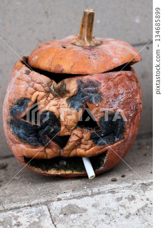 A decaying Halloween pumpkin sits on a concrete step, with a cigarette in its mouth. A decaying Halloween pumpkin sits on a concrete step, with a cigarette in its mouth. 134685899