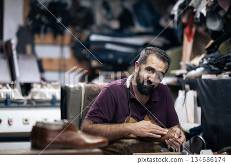 Cobbler at work in a busy leather workshop, crafting shoes with focus and care 134686174