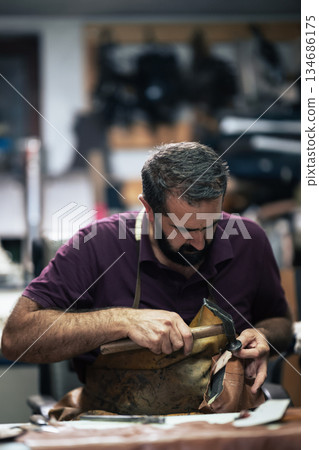Cobbler at work repairing a leather boot with a hammer in a busy workshop 134686175