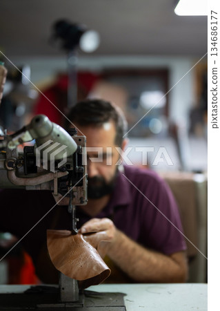 Leather craftsman sews a detailed boot on an industrial machine in a workshop Leather craftsman sews a detailed boot on an industrial machine in a workshop 134686177