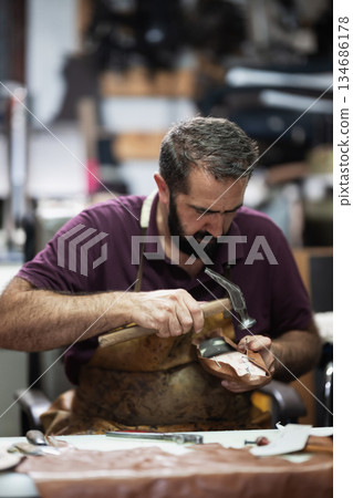 Craftsman hammering a leather shoe in a busy workshop, focusing on handmade footwear 134686178