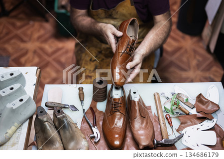 Cobbler at work crafting brown leather shoes with tools and materials on the table Cobbler at work crafting brown leather shoes with tools and materials on the table 134686179