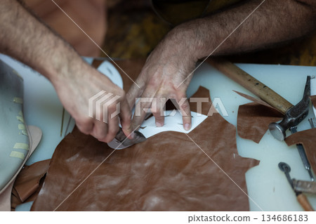 Leather worker shaping material with knife and tools on a worktable Leather worker shaping material with knife and tools on a worktable 134686183