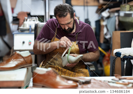 Skilled shoemaker at work measuring a leather shoe in a busy workshop Skilled shoemaker at work measuring a leather shoe in a busy workshop 134686184