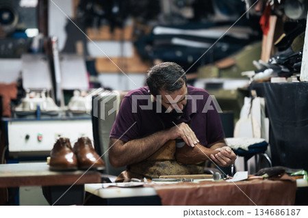 Cobbler at work polishing a leather boot in a busy workshop, focusing on craftsmanship Cobbler at work polishing a leather boot in a busy workshop, focusing on craftsmanship 134686187