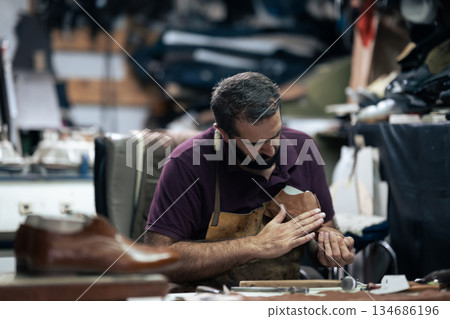 Skilled craftsman works on a leather shoe in a busy workshop, focused on handcrafting 134686196